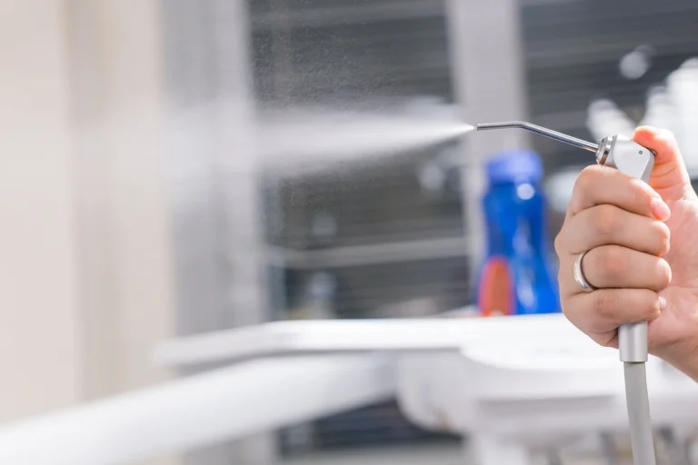 Odontologo ranka laiko burnos higienos purkštuvą, skirtą dantų valymui oro ir vandens srove